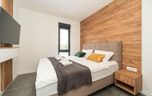 A modern bedroom with a wooden headboard, a bed with white linens, a grey blanket, and a nightstand with a wooden finish. - Beautiful apartment in Zadar (Zadar)