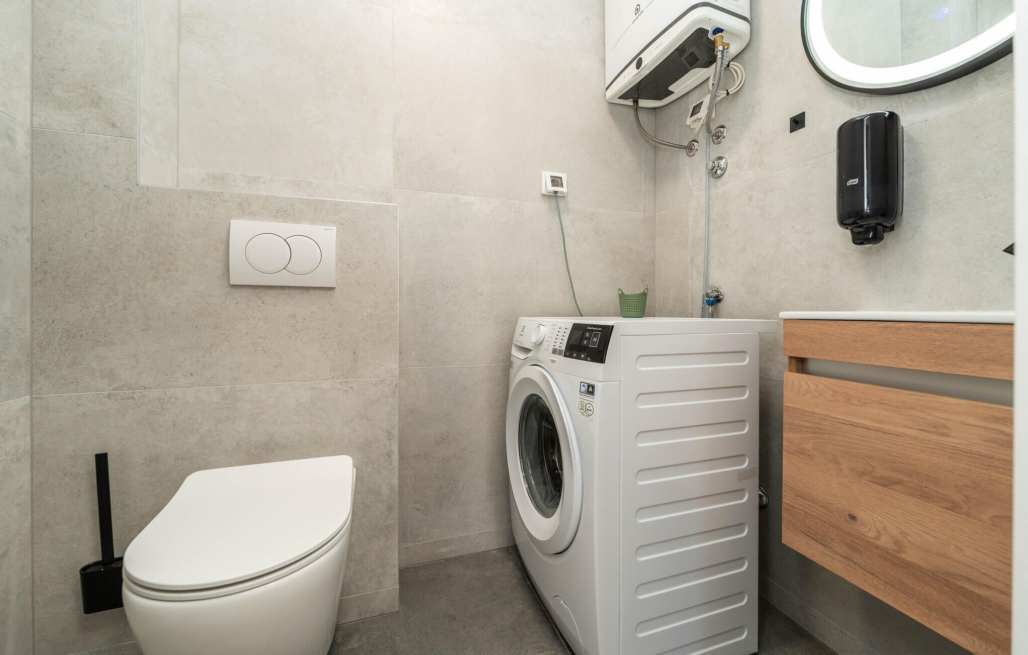 A modern bathroom with a toilet, washing machine, and wooden vanity.