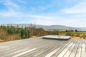 Een houten terras met een jacuzzi en een prachtig uitzicht op heuvels en velden.