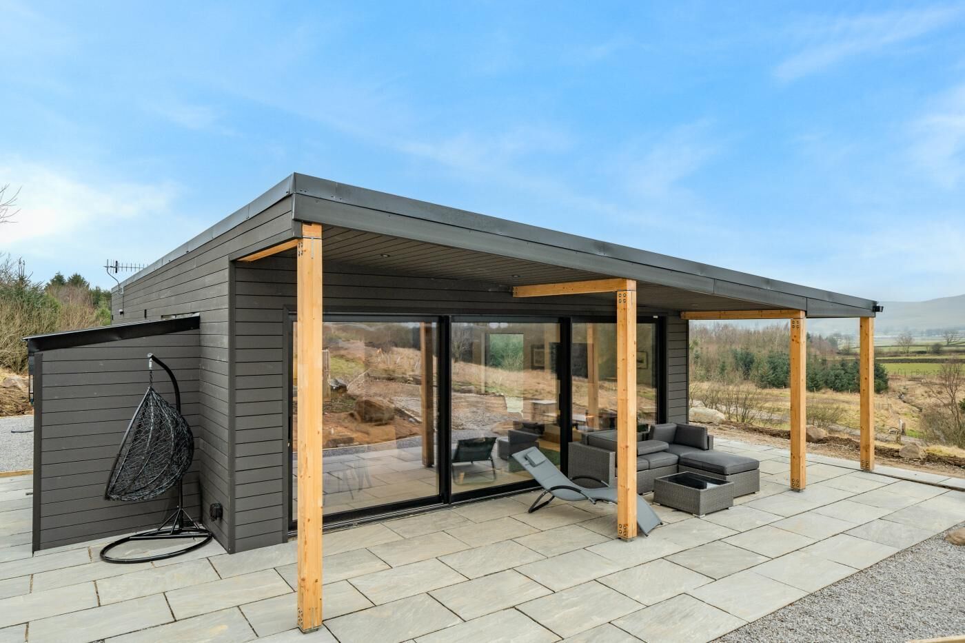 Una estructura moderna al aire libre con un área de estar techada, puertas de cristal amplias y un patio.