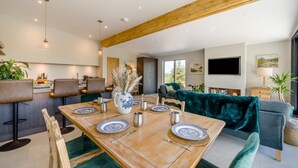 Una sala da pranzo moderna con un tavolo in legno apparecchiato per sei persone, circondato da sedie rivestite in verde.