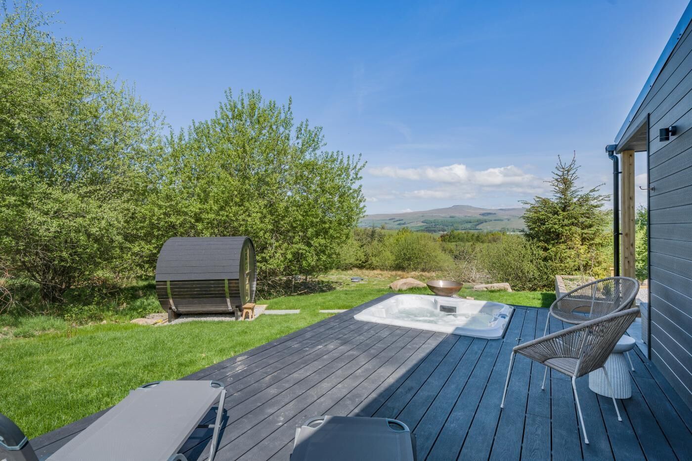Een terras met een jacuzzi, tuinmeubilair en een tuinhuisje in een tuin met een mooi uitzicht.