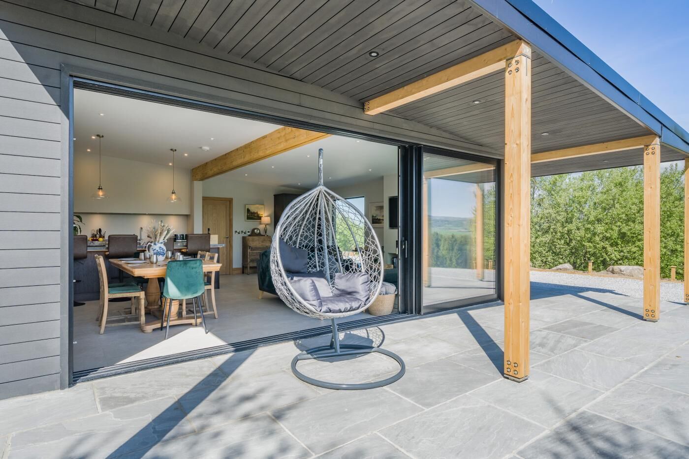 A modern house with a large glass door leading to a dining area and a hanging chair.