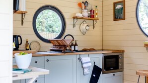 Eine kleine Küche mit rundem Fenster, Holzregalen, einer Mikrowelle und einem Wasserkocher.