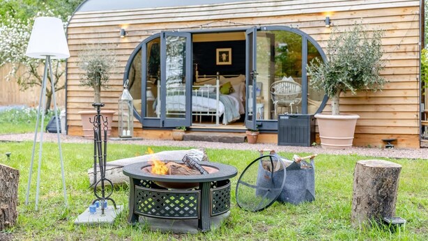 Ein gemütliches Mobilheim mit einer großen Glasschiebetür, einem Feuerkorb und Gartenmöbeln.