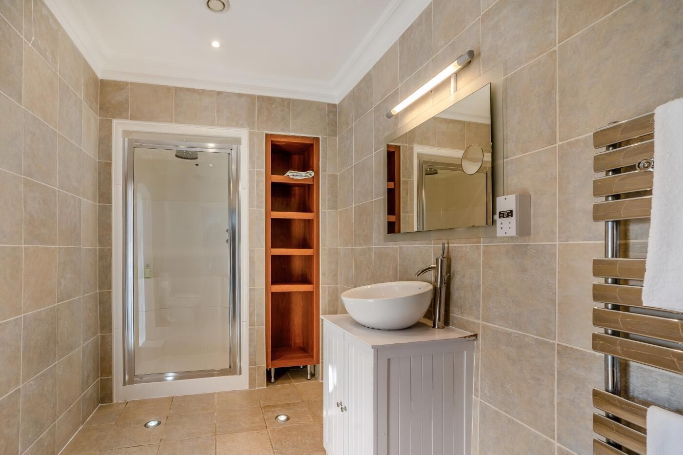 A modern bathroom with a glass shower enclosure, a built-in wooden shelf, a white sink with a chrome faucet, and a towel rack.