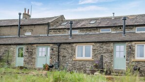 Une petite maison en pierre avec deux portes, un petit jardin et une cheminée.