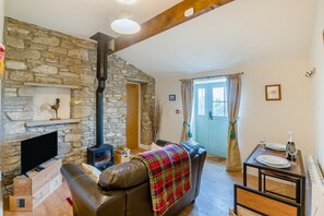 A cozy living room with a stone wall, a fireplace, a leather sofa, and a dining table with a bottle and glasses. - 1 Bed in Leyburn (oc-l30870) (Swineside)