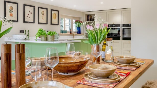 Eine moderne Küche mit Holztisch, gedeckt für ein Essen, inklusive Schüsseln, Gläsern und einer Vase mit Blumen.