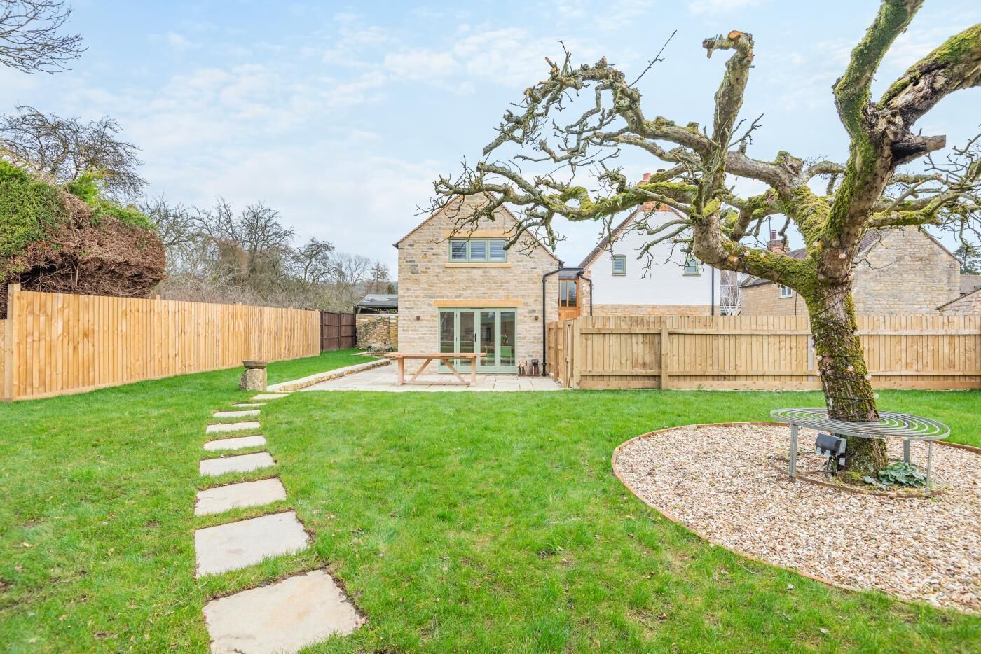 A backyard with a stone house, a wooden fence, a tree, and a gravel path.