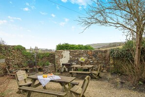 An outdoor seating area with wooden tables and benches, surrounded by stone walls and vegetation. - 4 Bed in Little Haven (oc-t30874) (Little Haven)