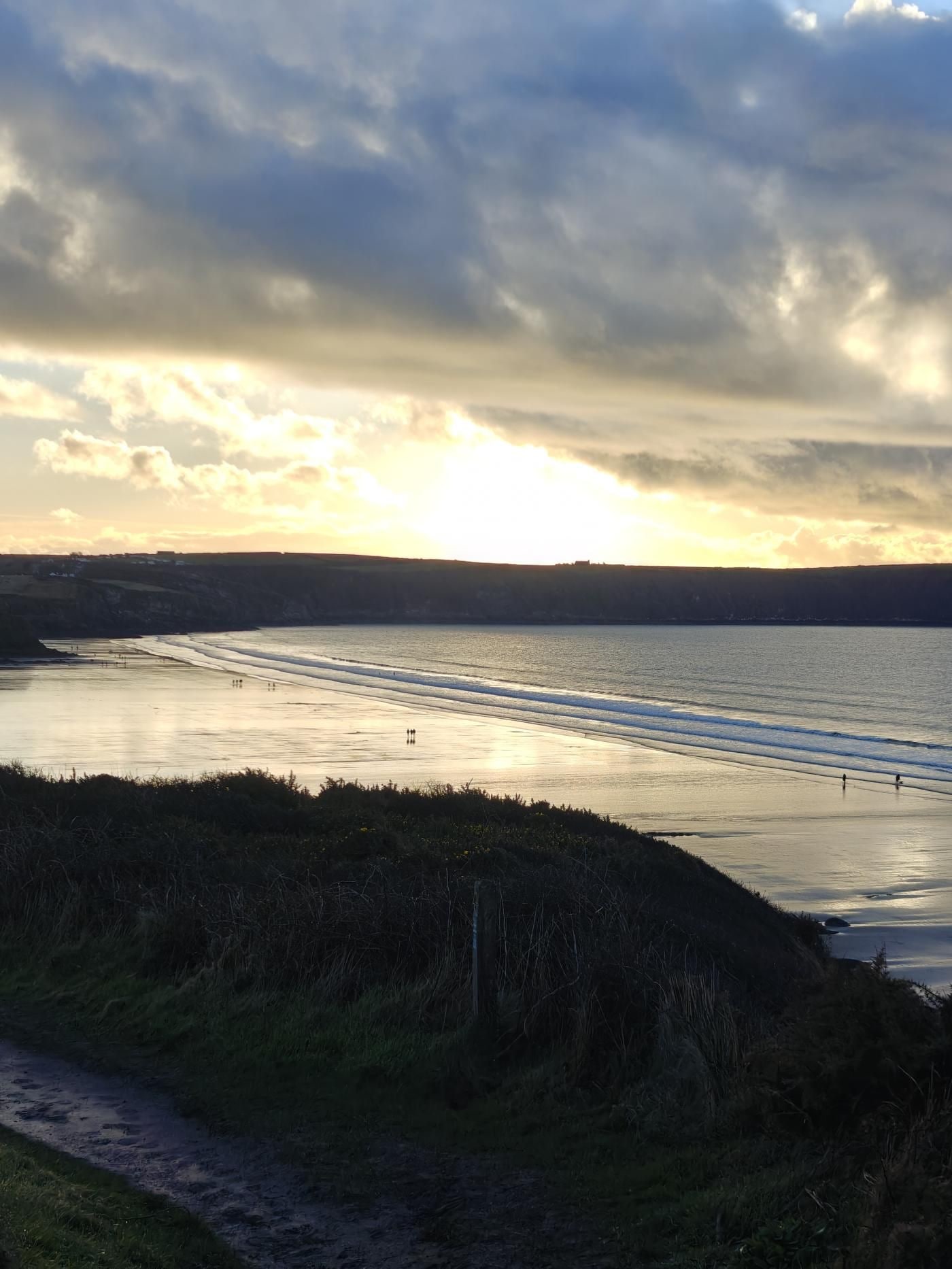 A coastal landscape with a path leading to the beach, a body of water, and a distant shoreline.