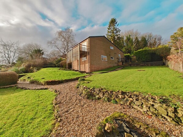 A modern house with a sloped roof, a wooden deck, and a well-maintained lawn. - 5 Bed in Tealby (oc-t30618) (Tealby)