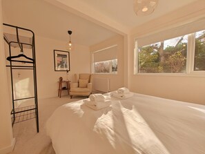 A bedroom with a large bed, a chair, a radiator, a window with a view, and a wall-mounted rack with hangers. - 5 Bed in Tealby (oc-t30618) (Tealby)