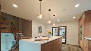 Uma cozinha moderna com ilha central, iluminação pendente, armários de madeira e uma escada para um andar superior.