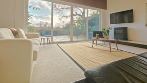 Uma sala de estar moderna com uma grande porta de vidro deslizante para um pátio, uma TV de tela plana na parede e uma lareira a lenha.