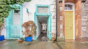 Une ruelle étroite avec un immeuble aux couleurs bleu et blanc, une porte jaune et des plantes en pot.