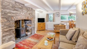 Un salon chaleureux avec une cheminée en pierre, un canapé en bois, une table basse et une vue sur l’extérieur par une fenêtre.