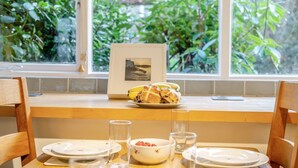 Une table à manger dressée avec des assiettes, un saladier de fruits et un tableau encadré.