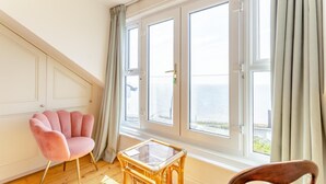 A room with a large window, a pink chair, a small table, and a wooden chair.