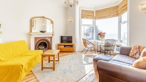 A living room with a fireplace, yellow sofa, brown leather sofa, wooden coffee table, and a bay window with curtains.