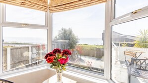 A room with a bay window overlooking a garden and a view of the sea.