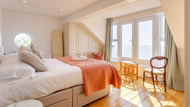A bedroom with a bed, a small table, a chair, and a window with curtains.