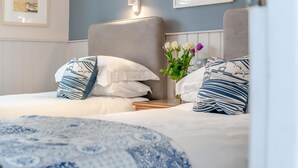 Quarto de hotel com duas camas, cada uma com almofadas estampadas e um vaso de flores.