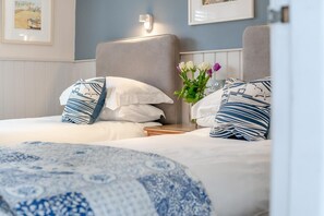 Habitación de hotel con dos camas, cada una con almohadas estampadas y un jarrón de flores.
