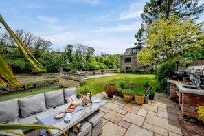 A patio with a table set for dining, a brick oven, and a stone building in the background. - 1 Bed in Little Petherick (oc-a30789) (Little Petherick)