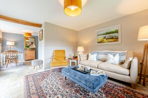 A living room with a sofa, armchair, and ottoman, a dining area with a table and chairs, and a kitchen area with a cabinet and counter.