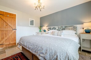 A bedroom with a bed, bedside tables, a nightstand, a chandelier, a wooden door, and a wall-mounted mirror.