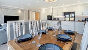 Een moderne keuken met witte kasten, een eethoek met een houten tafel gedekt voor zes personen, en een grijze bank op de achtergrond.