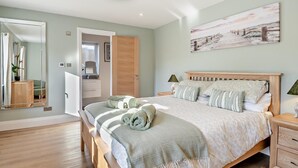 Een slaapkamer met een houten bed, een grote spiegel, een schilderij en een houten vloer.