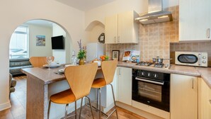 Een kleine keuken met een centraal eiland, barstoelen, een magnetron, fornuis, oven en een groot raam.