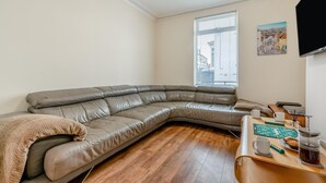 Een moderne woonkamer met een gebogen leren bank, een houten salontafel en een raam met zonwering.
