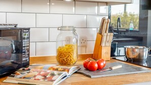 A kitchen counter with a pasta jar, tomatoes, a magazine, and kitchen utensils. - 4 Bed in Ringstead (oc-k30839) (Ringstead)