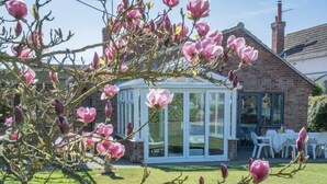A conservatory with a glass roof, surrounded by a brick house and a lawn. - 4 Bed in Ringstead (oc-k30839) (Ringstead)