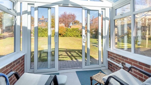 A conservatory with a glass door leading to a garden. Inside, there are two chairs and a small table. - 4 Bed in Ringstead (oc-k30839) (Ringstead)