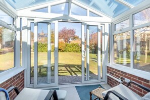 A conservatory with a glass door leading to a garden. Inside, there are two chairs and a small table. - 4 Bed in Ringstead (oc-k30839) (Ringstead)