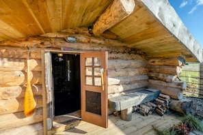Une cabane en rondins avec une porte en bois, un banc et une cheminée.