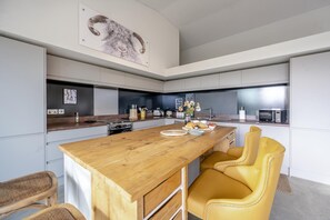 Une cuisine moderne avec un îlot central en bois, des chaises jaunes et un grand tableau accroché au mur.