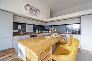 A modern kitchen with a wooden island, yellow chairs, and a large painting on the wall. - 3 Bed in Foulsham (oc-b30933) (Foulsham)