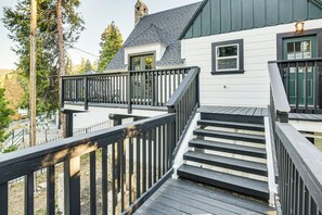 Una terraza de madera con una escalera que lleva a una casa con revestimiento blanco y techos oscuros.