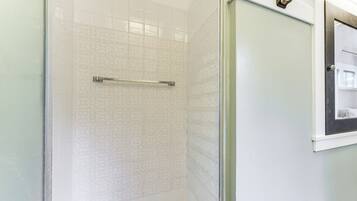 A bathroom with a glass shower enclosure, a towel rack, and a framed picture on the wall.