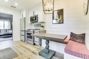 Una cocina moderna con armarios blancos, electrodomésticos de acero inoxidable, una mesa de comedor de madera y un banco con cojín a cuadros.