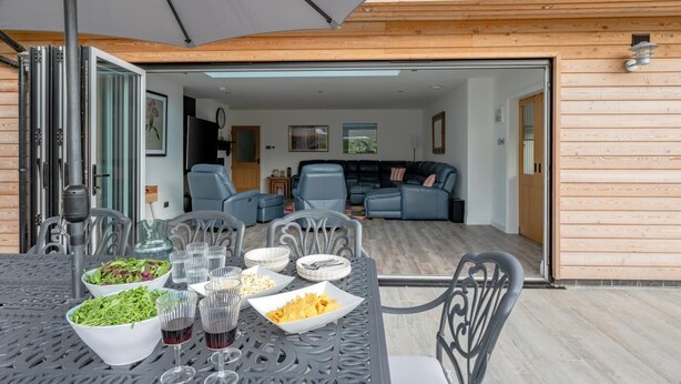 An open-plan living area with a dining table set for a meal, a sofa, and a kitchen visible in the background. - 5 Bed in Walberswick (oc-m30723) (Walberswick)