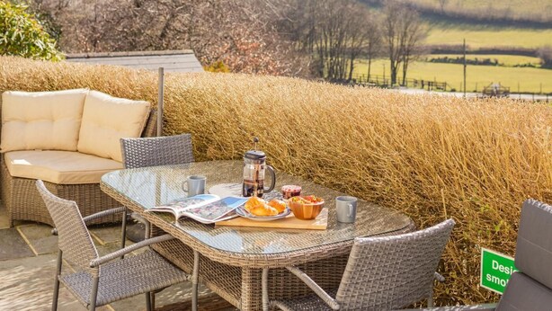A wicker outdoor seating area with a table set for breakfast, including a coffee pot, a bowl of fruit, and a croissant. - 2 Bed in Withypool (oc-c30940) (Withypool)