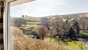 A view from a window overlooking a rural landscape with rolling hills, a small house, and a field. - 2 Bed in Withypool (oc-c30940) (Withypool)