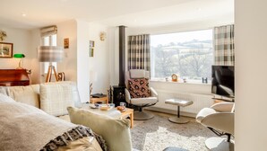 A modern living room with a sofa, armchair, and a television. There is a window with a view of the outdoors. - 2 Bed in Withypool (oc-c30940) (Withypool)